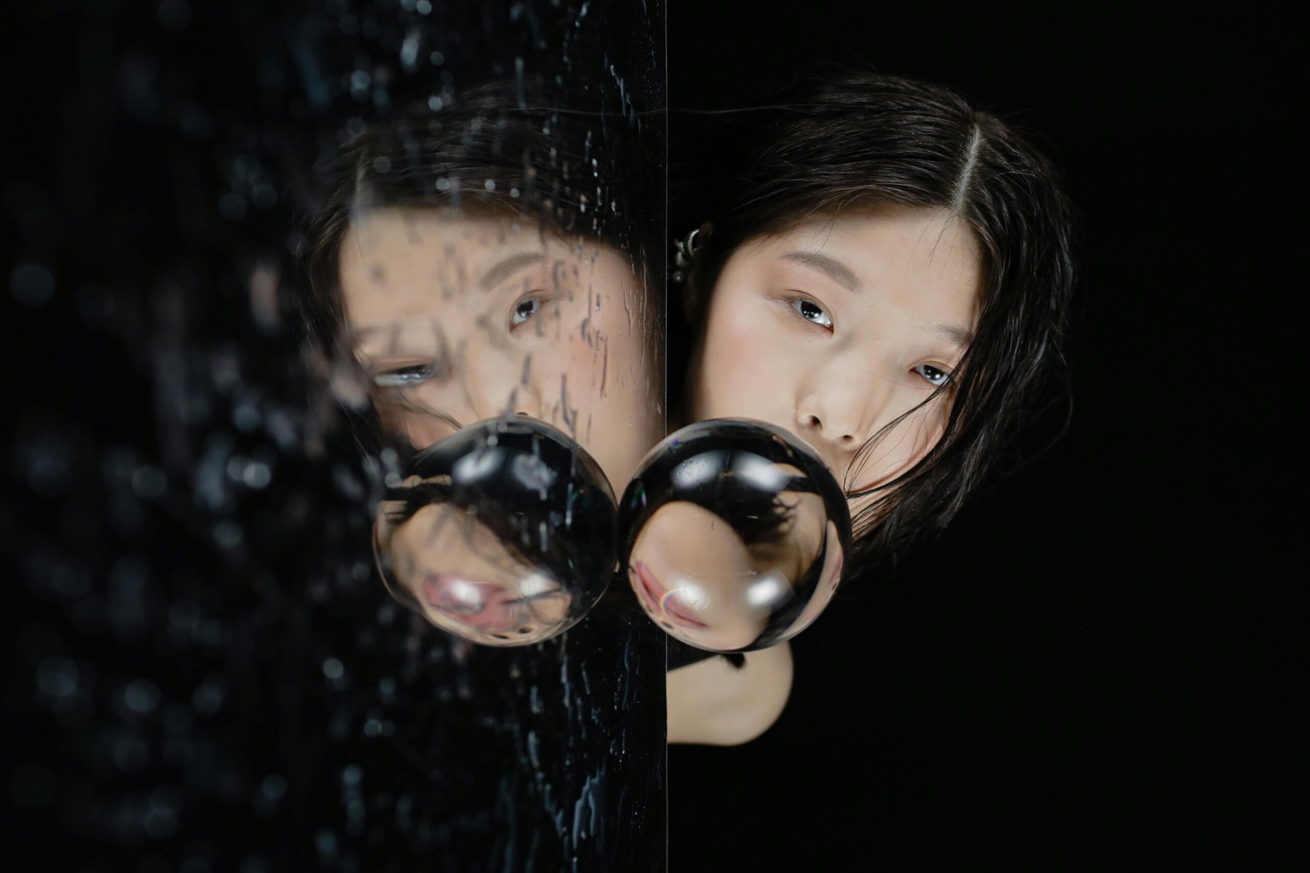 Woman gazing into a rain-splattered mirror with a distorted reflection, symbolizing deception, hidden truths, and emotional introspection.